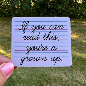 May include: White sticker with blue and pink lines. The sticker has cursive writing that says "If you can read this, you're a grown up."