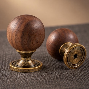 May include: Two spherical cabinet knobs featuring dark brown wood grain tops and antique brass-finished metal bases. One knob stands upright, while the other is positioned on its side, revealing the circular mounting plate and central screw hole.