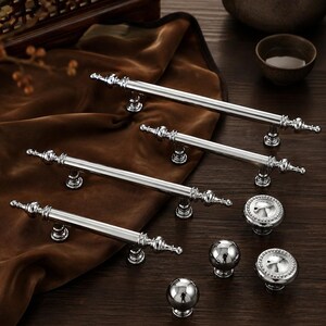 May include: A collection of polished silver-toned cabinet hardware including three elongated bar pulls with decorative finials and three round knobs, two of which feature a beaded edge detail and one that is a smooth, plain spherical shape.