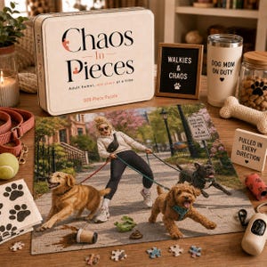 May include: A 500-piece jigsaw puzzle titled Chaos In Pieces featuring a scene of a person walking two dogs on leashes. The puzzle box is white with black text. Accessories include a tumbler labeled Dog Mom On Duty and a sign reading Pulled In Every Direction.