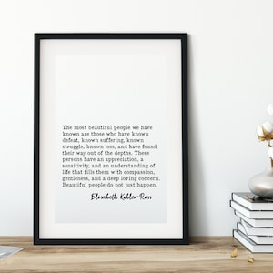 Op de afbeelding: Een zwart-wit ingelijste print met een citaat van Elisabeth Kübler-Ross over de schoonheid van mensen die lijden hebben ervaren. Het citaat luidt: "De mooiste mensen die we kennen zijn degenen die nederlagen hebben ervaren, die lijden hebben ervaren, die hebben gestreden, die verliezen hebben geleden en die hun weg uit de diepten hebben gevonden. Deze mensen hebben een waardering, een gevoeligheid en een begrip van het leven dat hen vult met mededogen, zachtaardigheid en een diepe, liefdevolle zorg. Mooie mensen gebeuren niet zomaar."