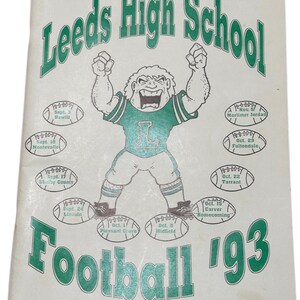 May include: A white Leeds High School Football 1993 program featuring green text and a central illustration of a mascot in a jersey with the letter L. Surrounding the mascot are ten football-shaped graphics listing game dates and opponent names.