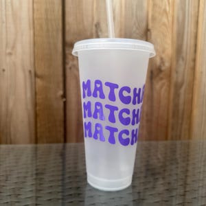 May include: A frosted translucent plastic tumbler with a matching lid and a clear straw. The cup features the word MATCH printed three times in a stacked, wavy purple font with a small heart icon integrated into the letter A of each word.