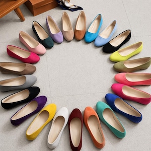 Könnte beinhalten: Eine Sammlung von vierundzwanzig flachen Schuhen, die in einem Kreis angeordnet sind und eine Vielzahl von Volltonfarben wie Schwarz, Weiß, Rot, Pink, Gelb, Blau, Grün, Lila, Orange, Braun und Grau aufweisen, alle mit einer glatten, matten Oberfläche.