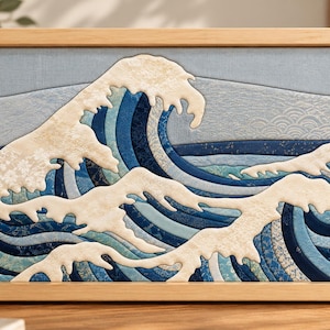 May include: A rectangular framed fabric wall art piece featuring a layered textile depiction of a large ocean wave. The design uses various shades of blue and cream-colored fabric with intricate patterns, set within a light wood frame.