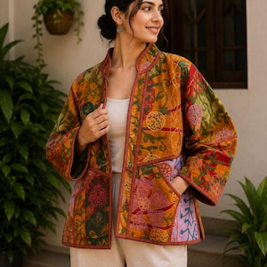 May include: A quilted jacket featuring a vibrant patchwork of mustard yellow, deep red, and soft lavender floral embroidery. This open-front garment includes a mandarin collar, long sleeves, and two front patch pockets with solid red trim.