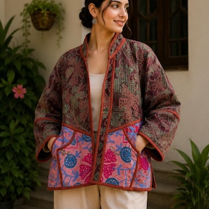 May include: A quilted jacket featuring a mandarin collar and long sleeves. The upper portion displays a dark brown and green floral pattern, while the lower section is pink with blue and magenta floral embroidery. It includes two front pockets.