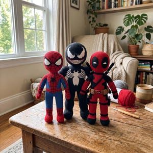 May include: Three handmade crochet dolls representing comic book characters. On the left, a red and blue Spider-Man figure. In the center, a black Venom figure with a white spider emblem. On the right, a red and black Deadpool figure with swords.