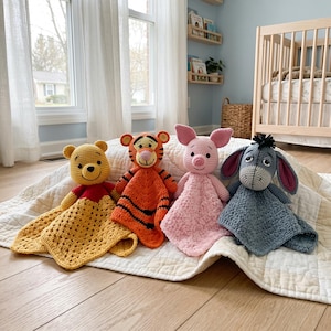 May include: Four crochet security blankets featuring Winnie the Pooh, Tigger, Piglet, and Eeyore. Each plush character is attached to a soft, textured, square-shaped blanket in colors matching the character: yellow, orange with black stripes, pink, and blue.