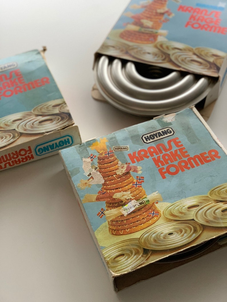 Op de afbeelding: Drie dozen met metalen taartvormen voor het maken van traditionele Noorse kransekake. De dozen zijn blauw en wit met de tekst "Kransekake Former" en het merk "Hoyang".