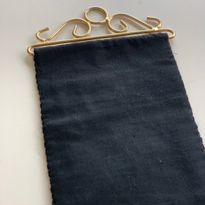 May include: A decorative wall hanging featuring a dark blue fabric panel suspended from a gold-colored metal frame. The frame has an ornate, scrolled design. The fabric has a textured appearance.