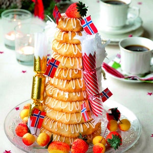 Op de afbeelding: Een traditionele Noorse kersttaart, genaamd Kransekake, is gemaakt van gestapelde ringen van amandelpasta en versierd met witte glazuur, kleine Noorse vlaggen en rood-witte pepermuntstokken. De taart is omringd door kleine rode en gele marsepeinvruchten en een enkele aardbei.