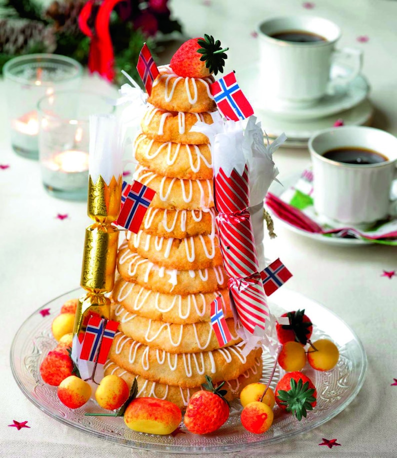 Op de afbeelding: Een traditionele Noorse kersttaart, genaamd Kransekake, is gemaakt van gestapelde ringen van amandelpasta en versierd met witte glazuur, kleine Noorse vlaggen en rood-witte pepermuntstokken. De taart is omringd door kleine rode en gele marsepeinvruchten en een enkele aardbei.