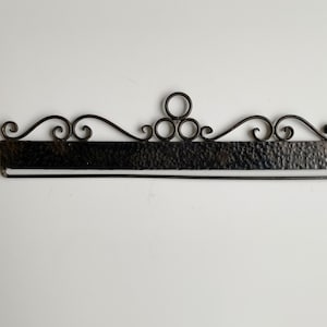 Puede incluir: Un colgador de pared de metal negro con un diseño decorativo de desplazamiento y una barra de metal martillado.