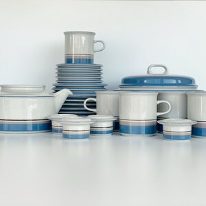 Puede incluir: Un juego completo de vajilla de cerámica blanca y azul. El juego incluye una tetera, tazas, platillos, una fuente para servir con tapa y hueveras. Cada pieza presenta un diseño de rayas azules y grises.