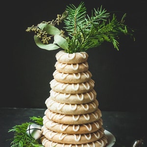 Op de afbeelding: Een traditionele Zweedse kerstcake, bekend als "lussekatten", is gestapeld in een piramidevorm en versierd met witte glazuur. De cake is bedekt met een takje groenblijvende plant.