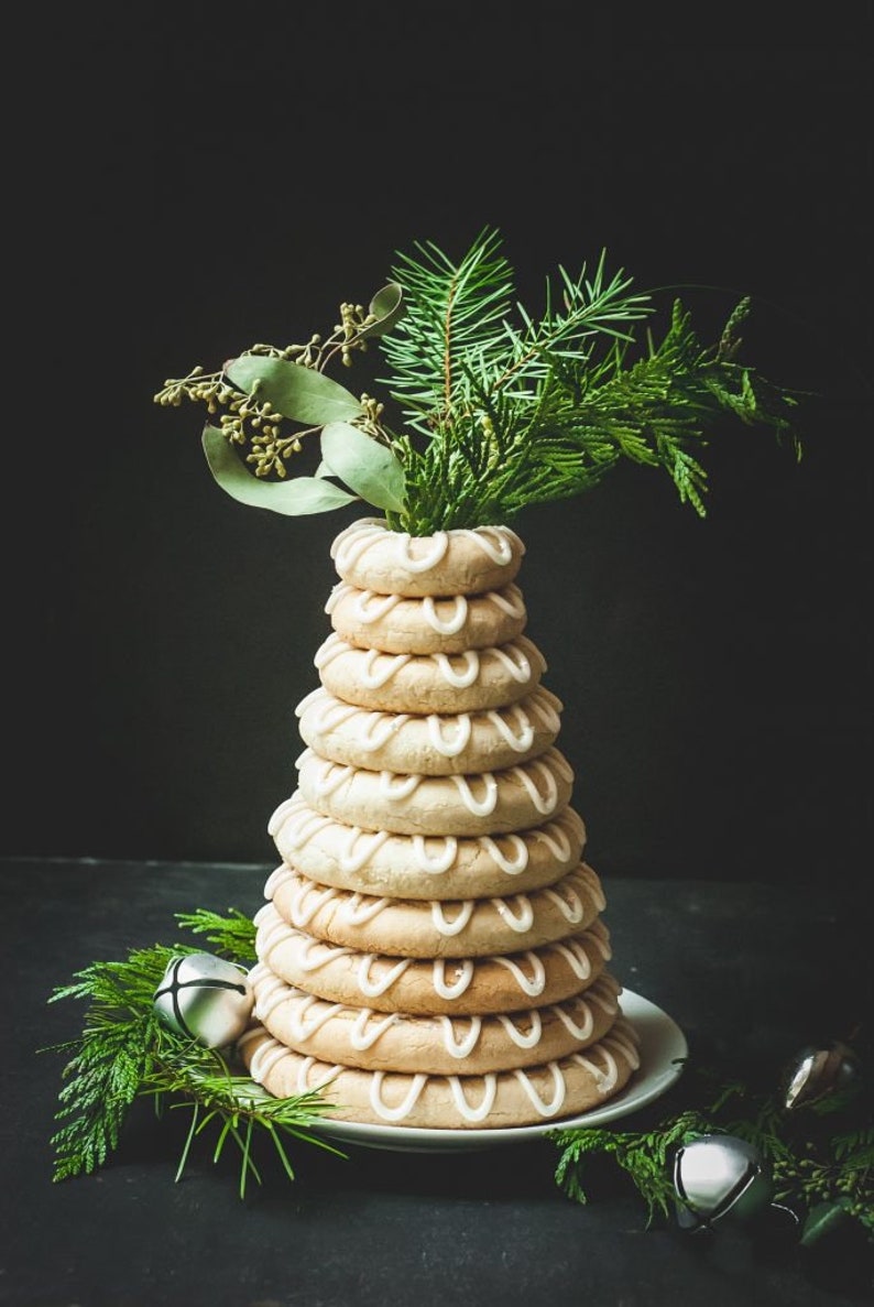 Op de afbeelding: Een traditionele Zweedse kerstcake, bekend als "lussekatten", is gestapeld in een piramidevorm en versierd met witte glazuur. De cake is bedekt met een takje groenblijvende plant.