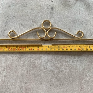 Pode incluir: Um cabide decorativo de metal dourado com um design curvo. O cabide mede aproximadamente 50 cm de comprimento e tem um anel na parte superior.