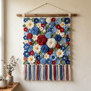 May include: A rectangular crochet wall hanging featuring a dense arrangement of three-dimensional red, white, and blue flowers and green leaves. The piece is suspended from a wooden dowel with a string and finished with long, multicolored yarn tassels.