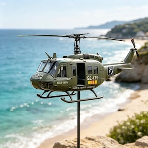 May include: An olive green model helicopter featuring the text VIETNAM VETERAN on the nose, 1055-1976 on the side, 58.479 near the door, and SERVICE-HONOR-SACRIFICE below. It includes a black rotor system, a tail rotor, and a black display stand.