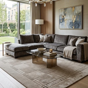 May include: A large, rectangular area rug featuring a textured, geometric pattern of raised horizontal and vertical lines in a neutral taupe color, positioned beneath a glass coffee table and a dark gray sectional sofa in a living room.