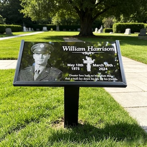 May include: A black granite memorial plaque on a metal stake featuring a portrait of a person in a military uniform, the name William Harrison, the dates 10th May 1975 and 18th March 2024, a cross icon, and the inscription Greater love hath no man than this.