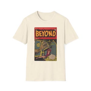 以下が含まれることがあります： クリーム色の半袖Tシャツで、The Beyondというタイトルのヴィンテージコミックの表紙がグラフィックプリントされています。イラストには、大きな手がベルを掴み、そのベルに人がぶら下がっている様子が描かれており、That monster, he's trying to kill me! Help! Help! I can't hold on much longer!というテキストが含まれています。