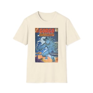 May include: A cream-colored short-sleeve t-shirt featuring a graphic print of a vintage comic book cover titled GORGO. The illustration depicts a large blue monster emerging from the ocean near a submarine, with orange and blue color tones.