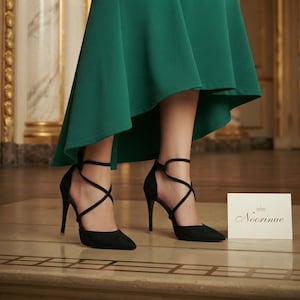 May include: A pair of black pointed-toe high heels with thin crisscross ankle straps and a green high-low skirt. A small white rectangular card is placed next to the shoes, featuring the text Noorinae with a small crown icon above the name.
