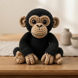May include: A crocheted chimpanzee stuffed animal featuring a black body with tan-colored hands, feet, ears, and face. The toy has large, round black eyes and a stitched mouth, crafted with a textured yarn finish in a seated, upright position.