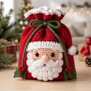 Peut inclure: Un sac à cordon en crochet rouge représentant un visage de Père Noël avec une barbe, une moustache et un bord de bonnet blancs. Le sac est resserré par un cordon en crochet vert noué, orné de petites feuilles de houx et de baies rouges.