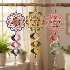 May include: Three hanging crochet ornaments featuring circular floral mandalas with intricate petal details. Each piece includes a spiraling tail and a clear crystal bead at the bottom. The color palettes include purple, yellow-green, and pink-teal.