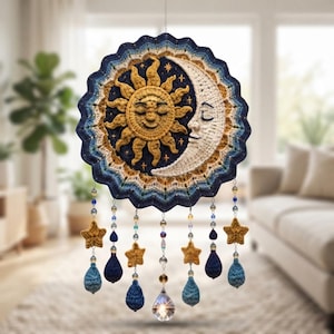 Op de afbeelding: Een ronde gehaakte wandhanger met een centraal zon- en maansikkelontwerp in geel en crème op een donkerblauwe achtergrond. Daaronder hangen meerdere strengen met kralen, kleine gehaakte sterren, druppelvormen en een heldere kristallen hanger.