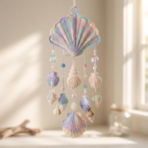 May include: A hanging mobile featuring a large crocheted pastel seashell at the top, adorned with dangling strands of smaller crocheted shells in shades of blue, pink, and cream, interspersed with clear, iridescent, and pearl-like beads.