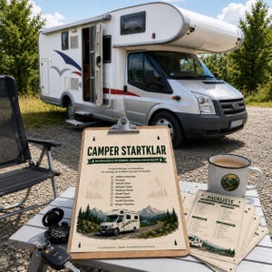 May include: A clipboard with a printed checklist titled CAMPER STARTKLAR featuring a camper van illustration, mountain graphics, and checkboxes. Beside it sits a white enamel mug with a camper graphic, a stack of matching checklists, and a black key fob.