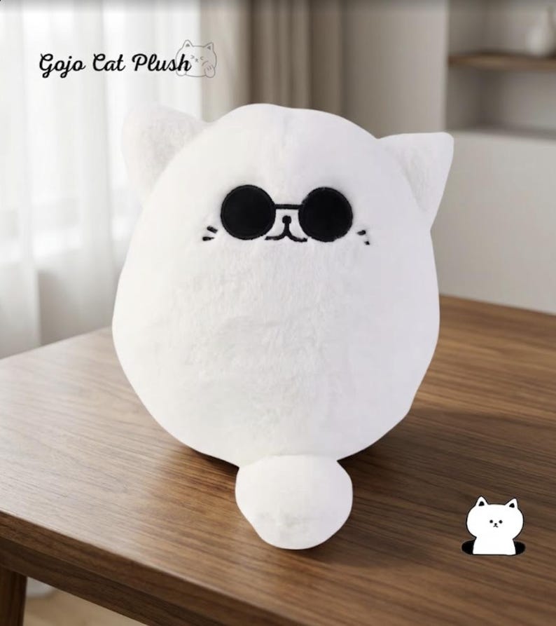 May include: A round white plush toy shaped like a cat with pointed ears and a small tail. The cat features embroidered black circular sunglasses, a small nose, and whiskers. The text Gojo Cat Plush is visible in the upper left corner.