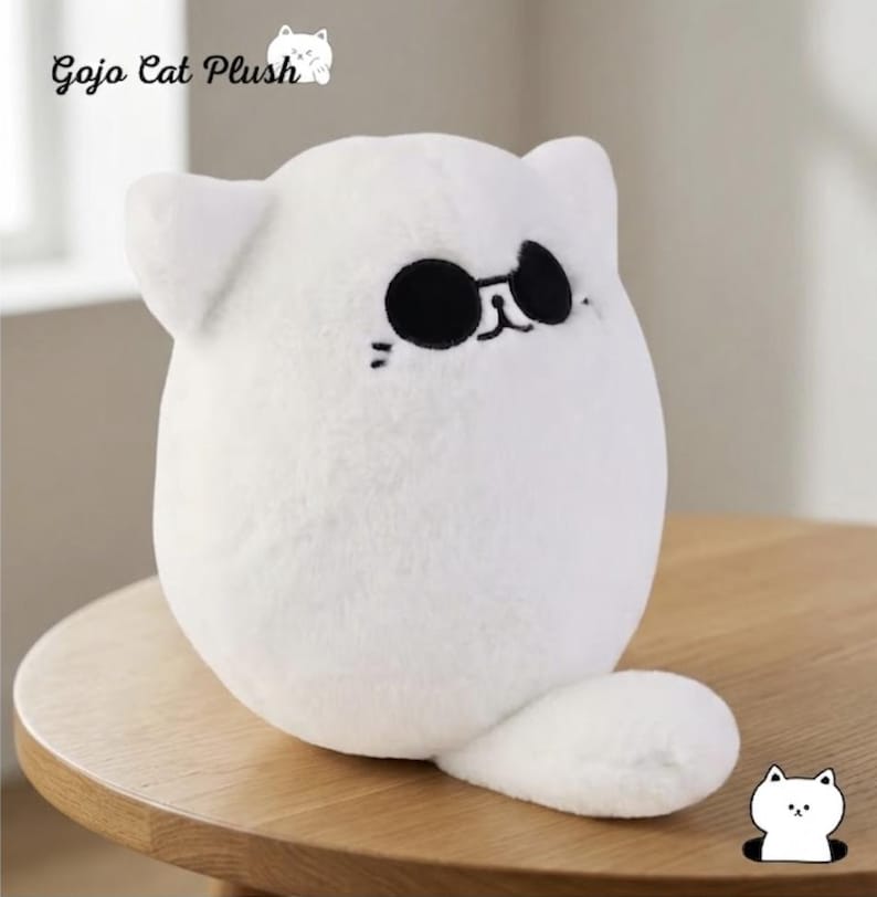May include: A white plush cat toy with a rounded body, pointed ears, and a small tail. The cat features embroidered black sunglasses, a simple nose, and whiskers. The text Gojo Cat Plush is visible in the upper left corner of the image.