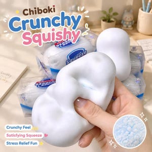 Könnte beinhalten: Ein weißes, wolkenförmiges Squishy-Spielzeug mit einer weichen, strukturierten Oberfläche. Die Verpackung trägt den Text Chiboki Crunchy Squishy und Squeeze. Ein kreisförmiger Einsatz zeigt eine Nahaufnahme des blauen, körnigen Füllmaterials.