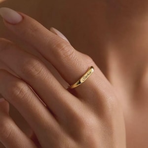 Peut inclure: Une bague anneau en or poli présentant une surface lisse et arrondie avec le nom Sephia gravé dans une police cursive. La bague possède une finition métallique réfléchissante et est portée sur un doigt, mettant en valeur le lettrage sombre.