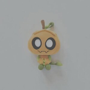 May include: A small, stylized plush figure shaped like a pumpkin with a light orange head, large white circular eyes, and a thin dark brown mouth. The body is light green with small arms and legs, and a green stem extends from the top of the head.