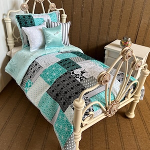 May include: A white metal doll bed with a teal and black patchwork quilt. The bed has a decorative headboard and footboard with ornate details. The quilt has a variety of patterns, including floral, geometric, and paisley.