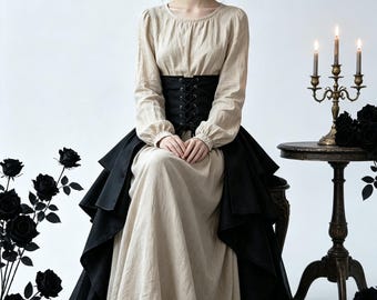 May include: A long-sleeved beige dress featuring a round neckline and a black corset-style waist cincher with front lacing. The dress includes a layered black overskirt that drapes over the floor-length beige skirt, creating a high-low silhouette.