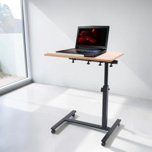May include: A portable laptop desk with a light wood-grain rectangular surface and a black metal frame. The desk features an adjustable height mechanism with visible knobs and a base equipped with four small wheels for mobility.