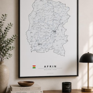 May include: A framed wall art print featuring a detailed black and white map of Afrin. The print includes the text "AFRIN" and "NAVÇA EFRÎNÊ ROJAVA" along with a small flag icon. The map displays intricate road networks and geographical boundaries.