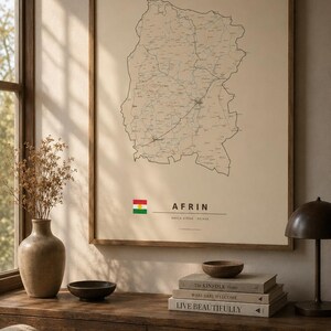 May include: A framed wall art print featuring a detailed black line map of Afrin on a beige background. Below the map, the text reads AFRIN, NAVÇA EFRÎNÊ, ROJAVA, accompanied by a small rectangular flag with red, white, and green horizontal stripes.