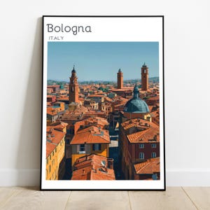 May include: A framed wall art print featuring a panoramic illustration of the city of Bologna, Italy. The image displays terracotta-colored rooftops, a prominent blue dome, and tall towers under a clear blue sky. The text reads Bologna ITALY.