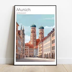 Puede incluir: Una lámina de arte mural enmarcada con una ilustración estilizada de Múnich, Alemania. La imagen muestra una calle que conduce a la Frauenkirche con sus dos icónicas torres de cúpula de cebolla, rodeada de edificios en tonos pastel.