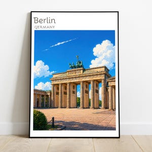 May include: A framed wall art print featuring the Brandenburg Gate in Berlin, Germany. The image shows the neoclassical monument with its columns and quadriga sculpture under a bright blue sky with white clouds. The text reads Berlin GERMANY.