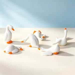May include: A collection of six white ceramic goose figurines with orange beaks and feet. The geese are depicted in various poses, including standing, resting, and stretching their wings, showcasing smooth surfaces and simple, rounded forms.