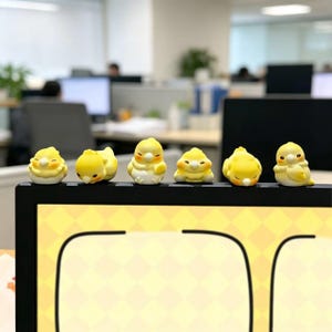 以下が含まれることがあります： 白いお腹とオレンジ色の頬の模様を持つ、6体の黄色い小鳥の形をした小さなフィギュアが、黒いコンピューターモニターの上端に一列に並んでいます。それぞれのフィギュアは異なるポーズをとっており、目を閉じているものや前を向いているものがあります。